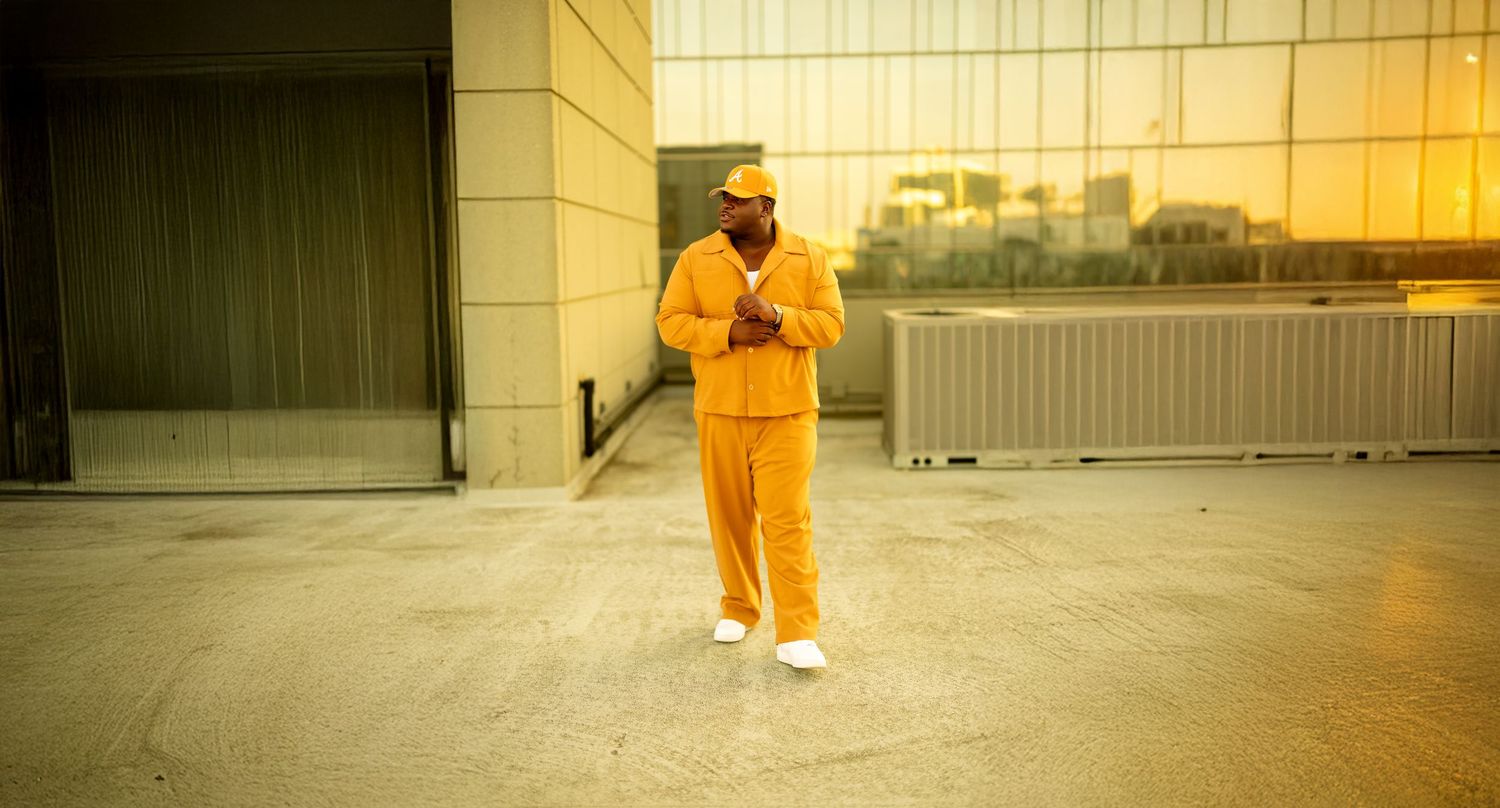 Person in bright orange jumpsuit walking through a modern building with reflective glass walls and industrial aesthetic.