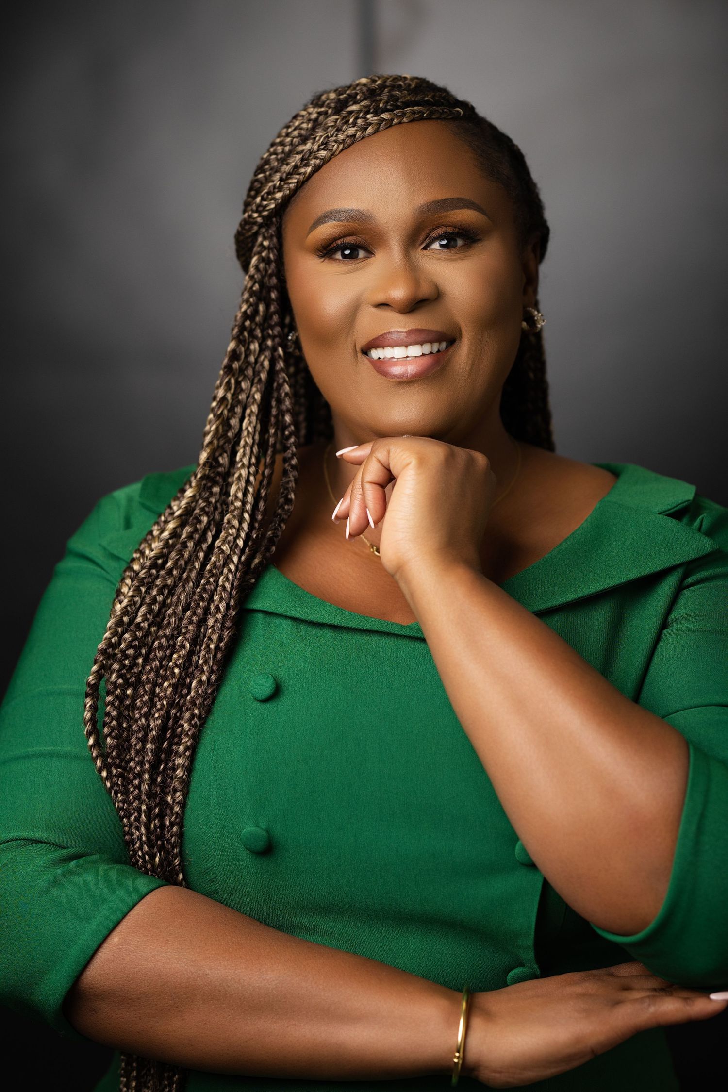 Professional studio portrait in emerald green dress against dark background.