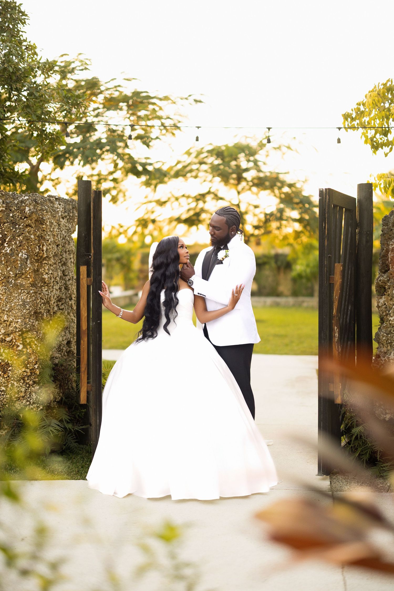 A couple in formal wedding attire dances together in a garden setting during golden hour.