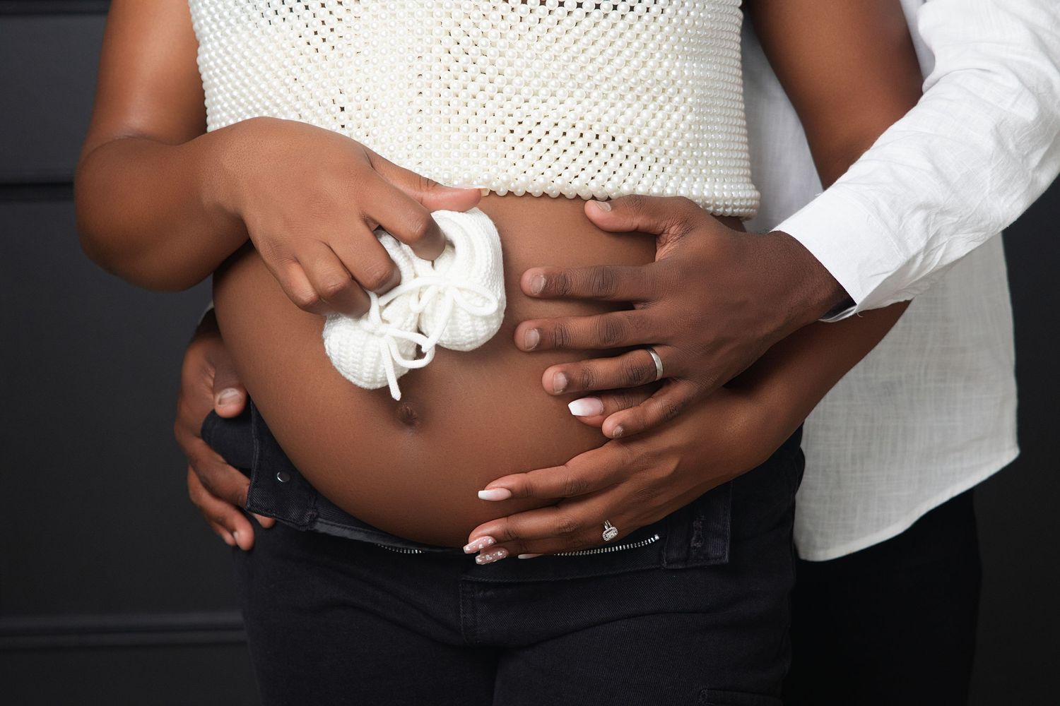 A pregnant person's belly is shown with hands placed lovingly on the exposed stomach against a dark background.