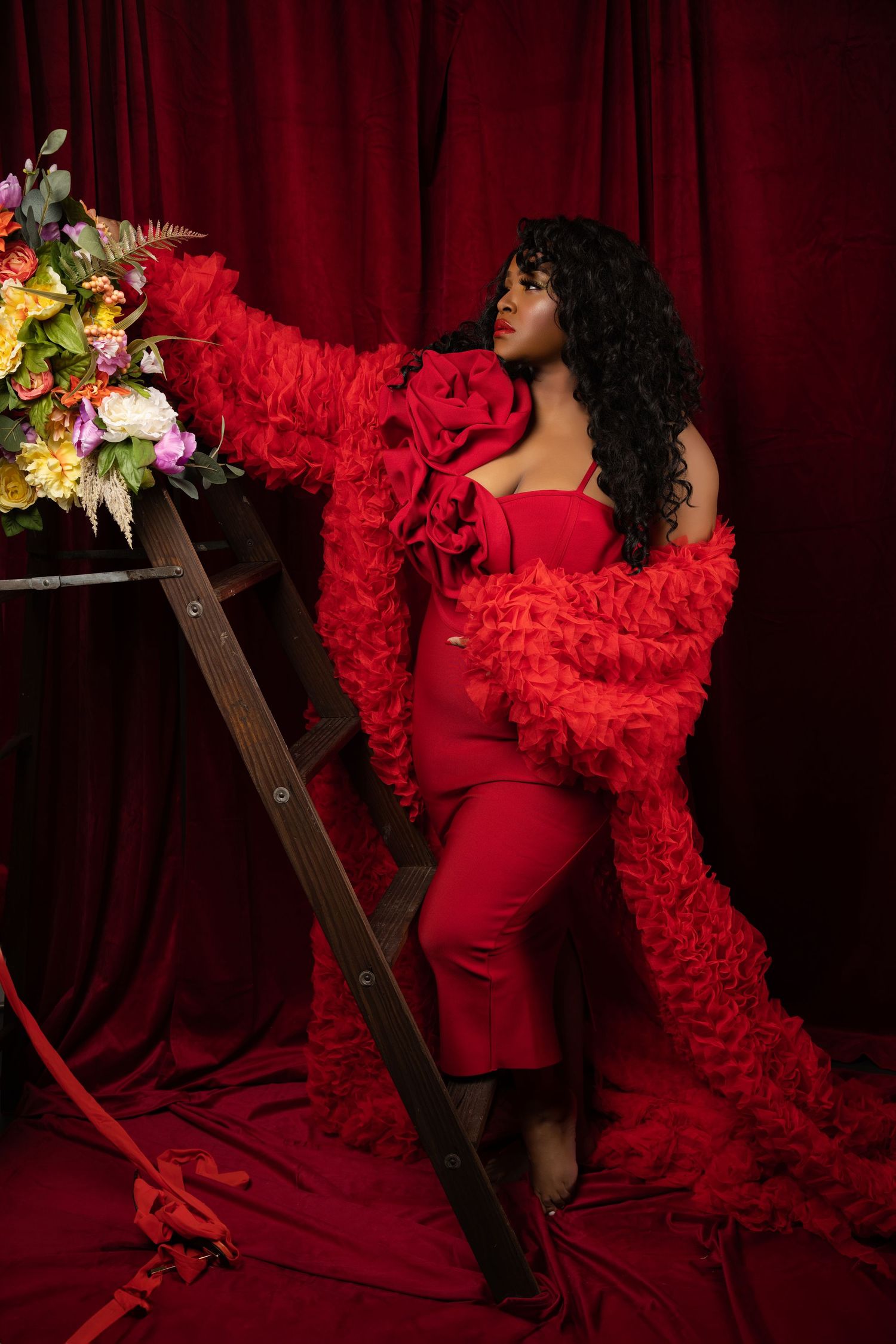Dramatic fashion shoot with flowing red ruffled dress against dark red velvet backdrop.