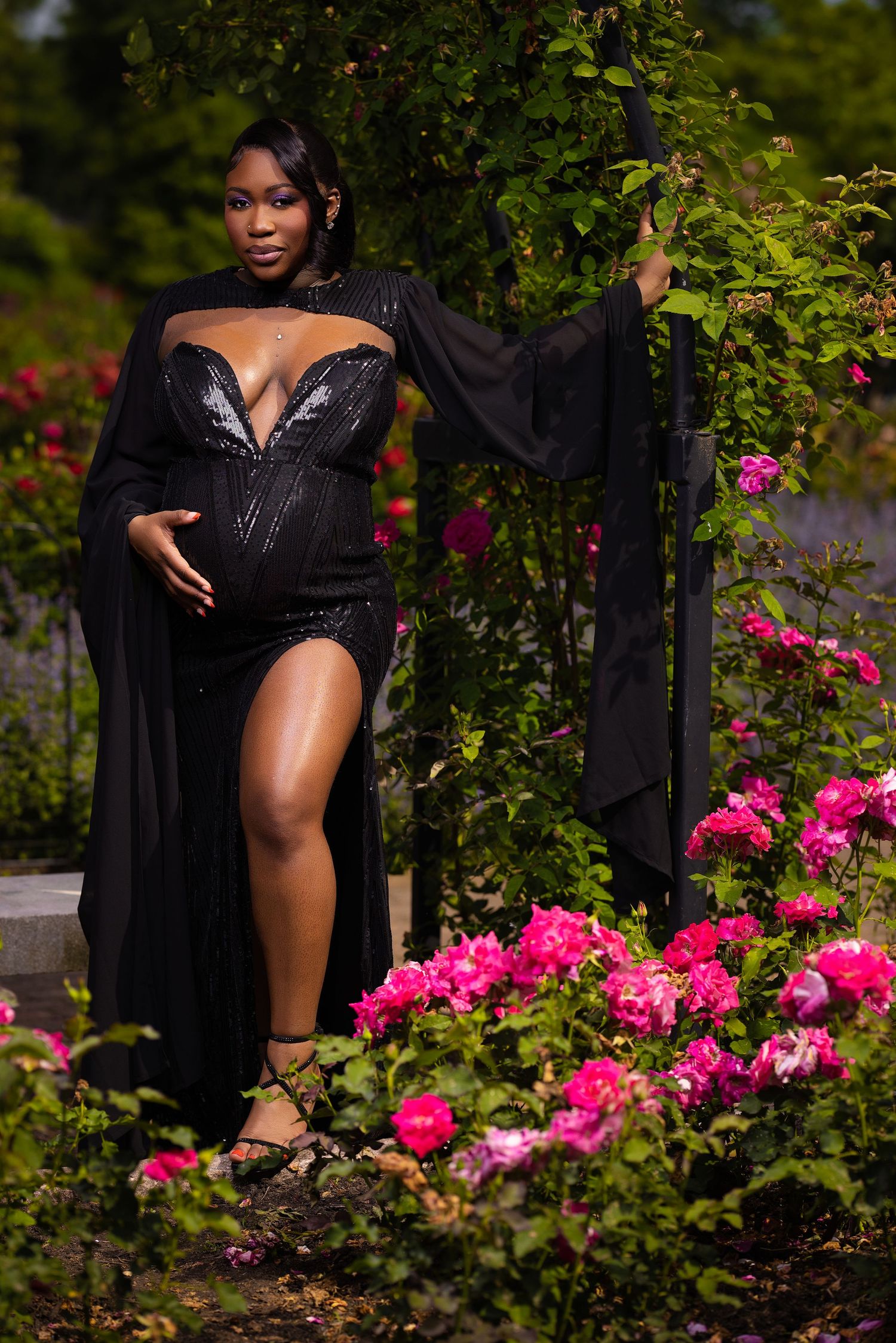 A glamorous fashion photoshoot in a garden with vibrant pink roses and dark foliage creating a dramatic backdrop.