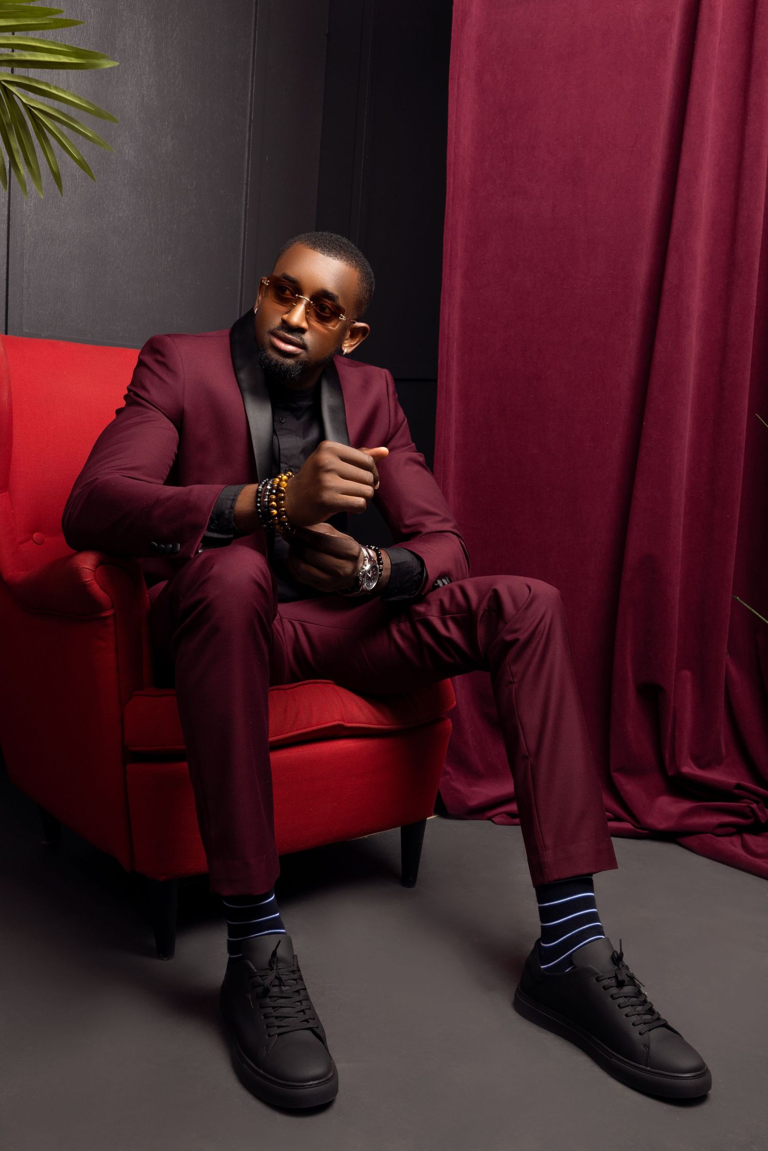 Stylish portrait of someone in burgundy suit sitting on red couch in moody lighting.