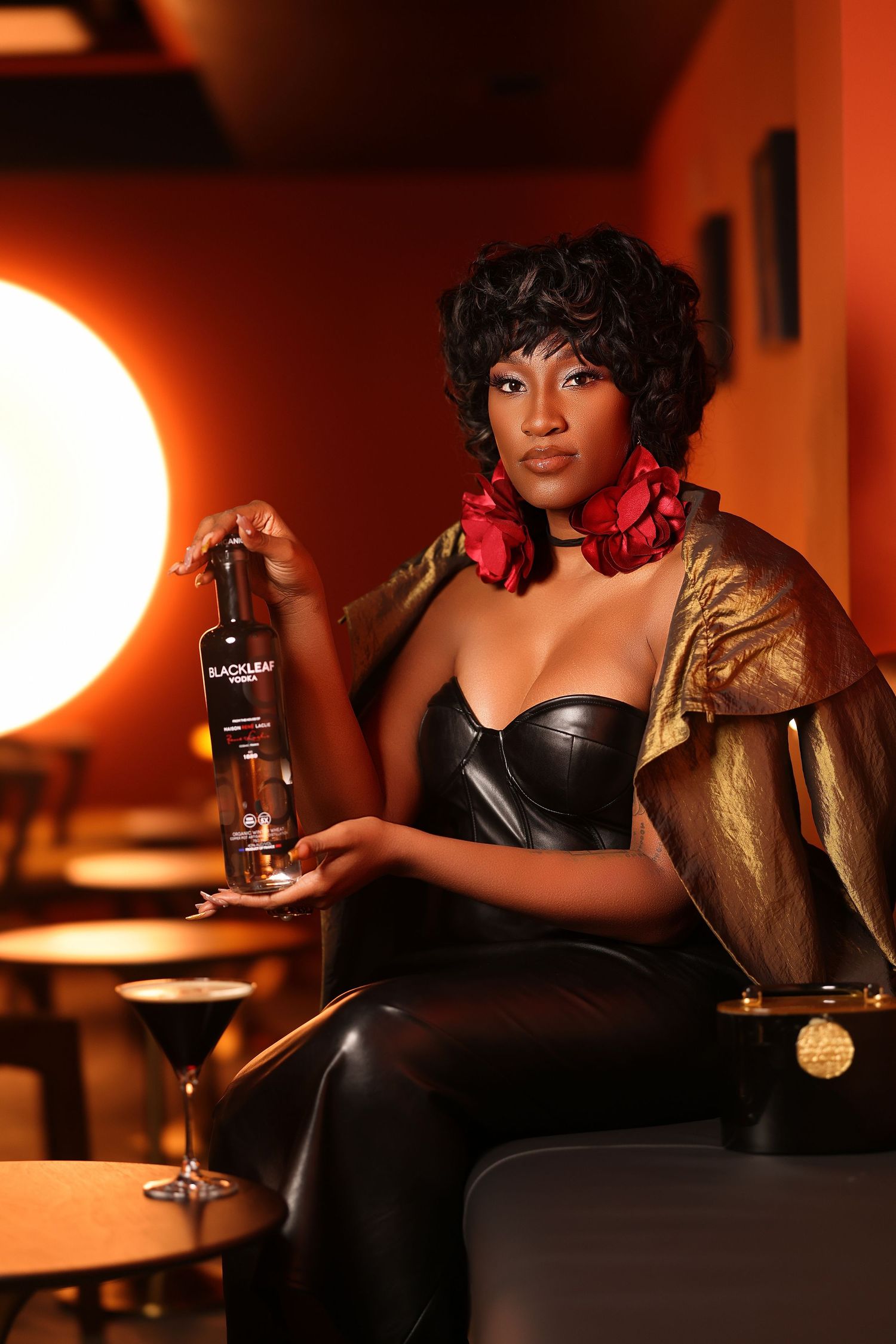 Moody bar scene with Black Leaf vodka bottle and cocktail glass in warm lighting.