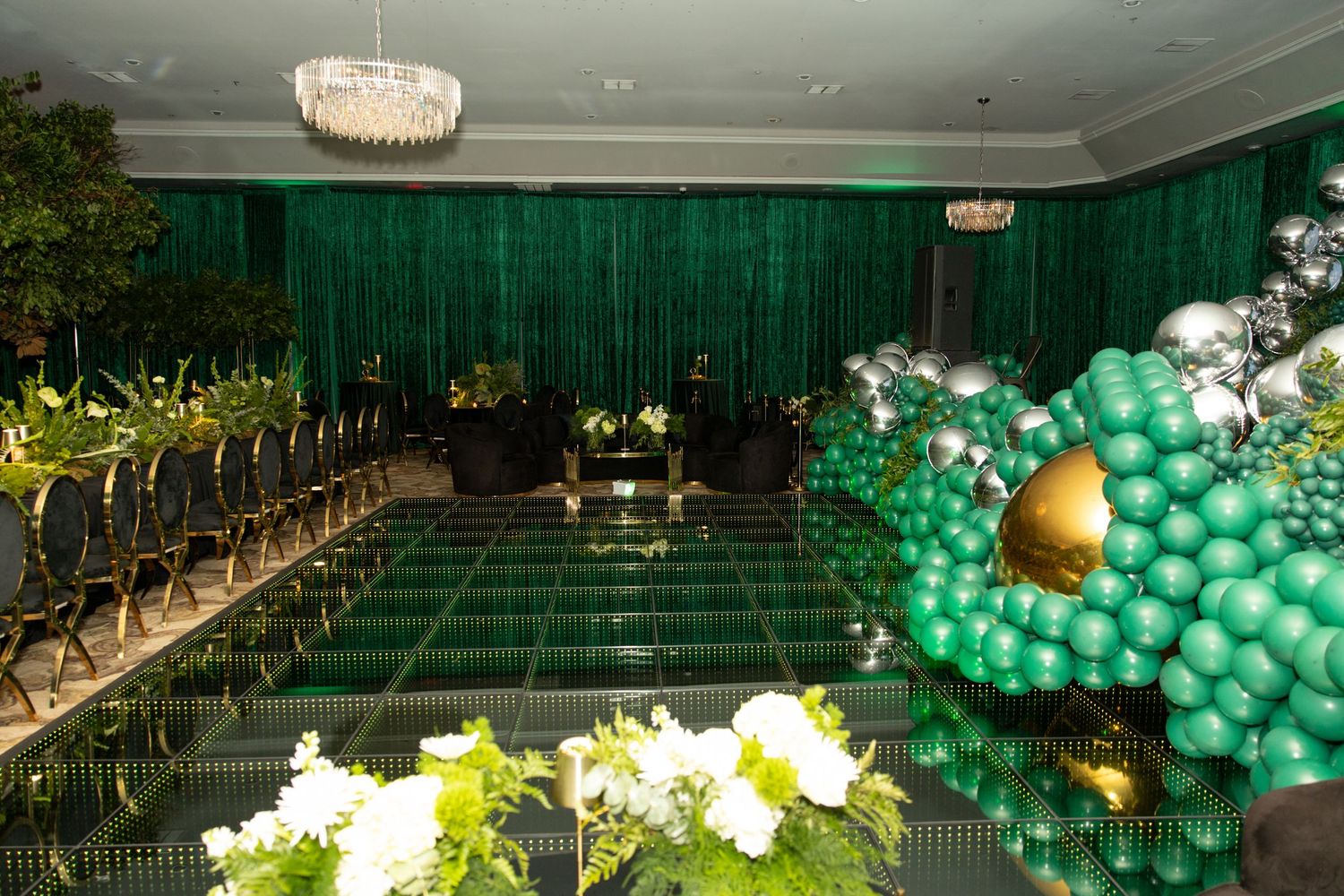 Luxurious event space with crystal chandelier, green draping, and elaborate balloon installations.