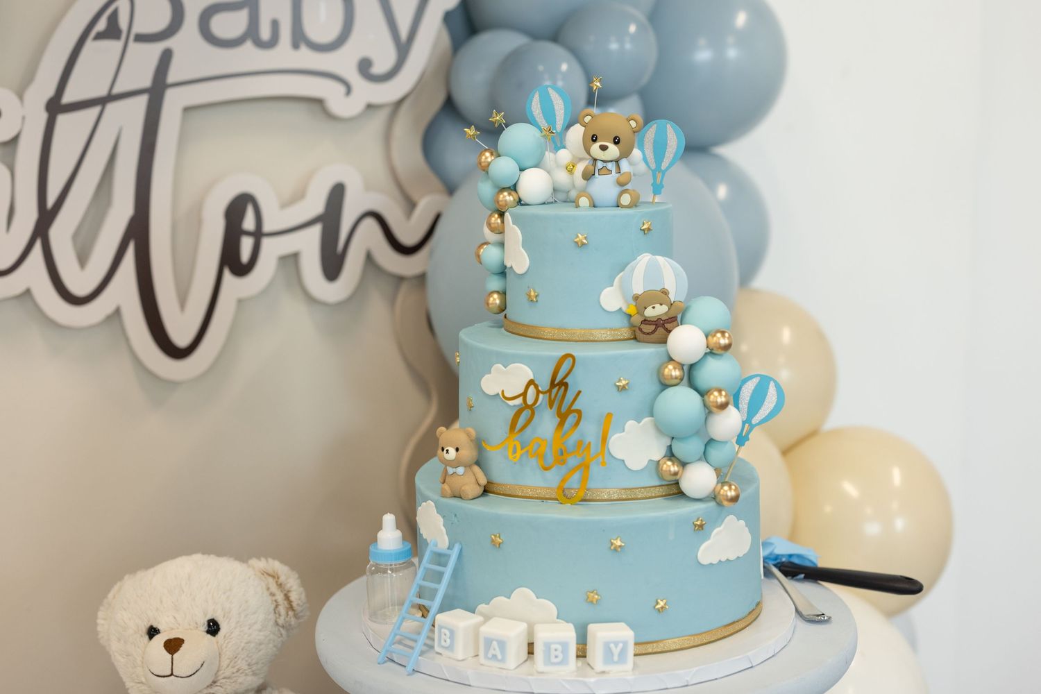 Blue and gold teddy bear themed baby shower cake with delicate decorations.