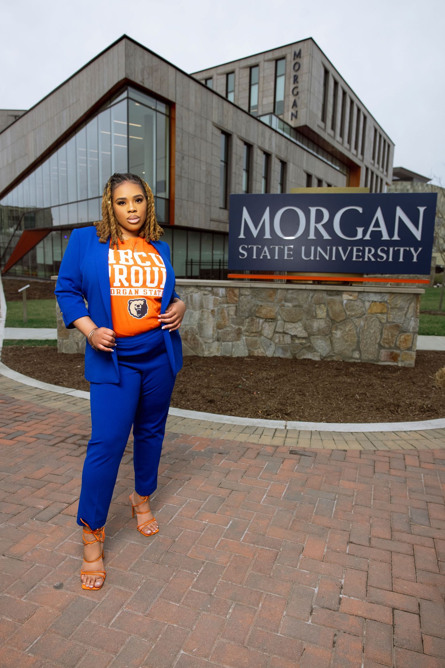 A student stands in front of the Morgan State University sign and modern campus building wearing bright blue attire.