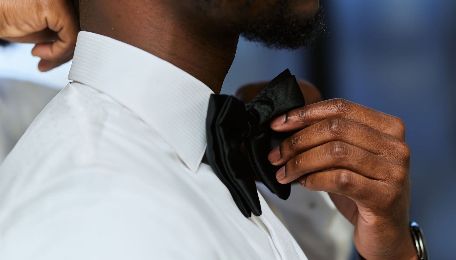 Close-up view of hands adjusting a black bow tie against a white dress shirt.