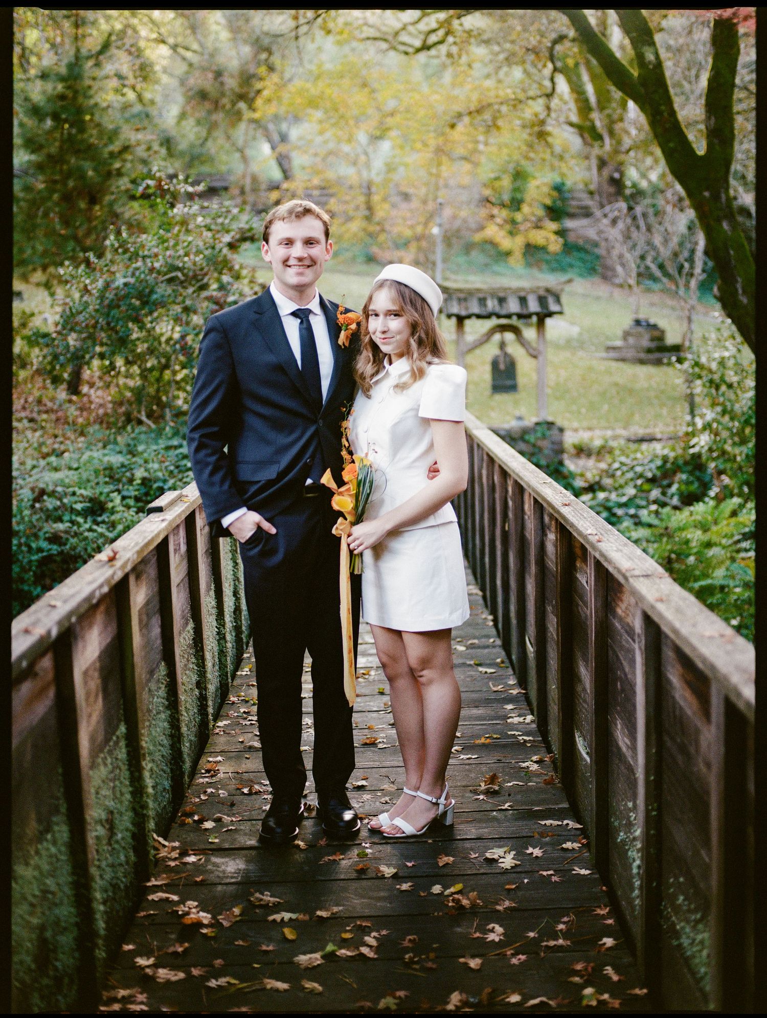 Bride and groom standing on bridge surrounded by greenery.