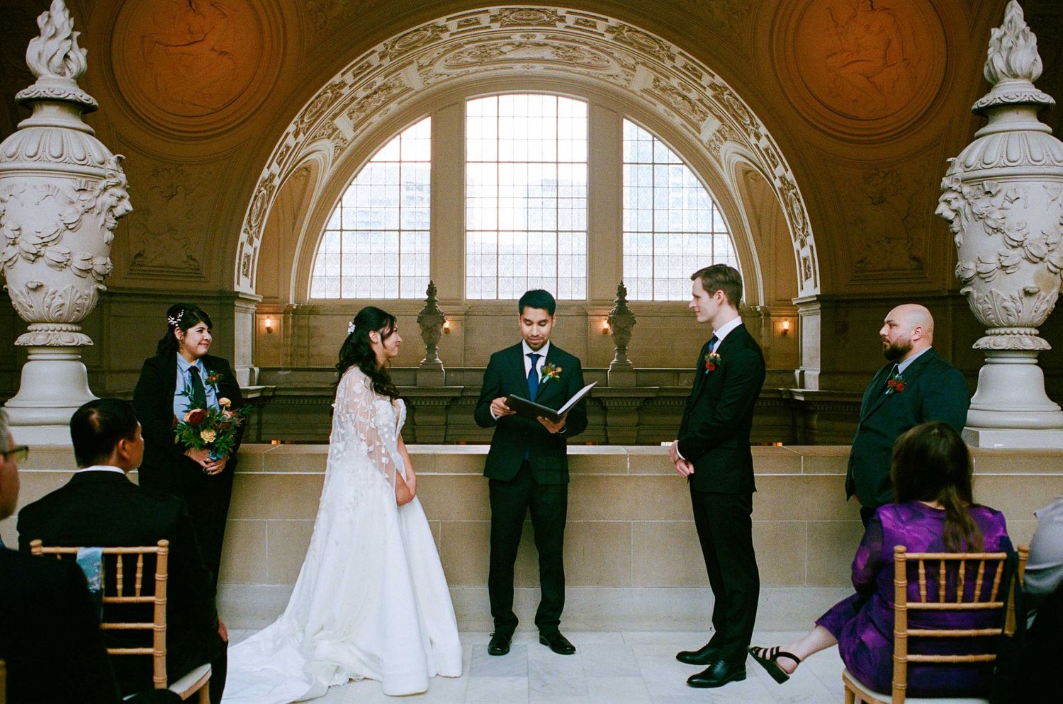 Wedding ceremony taking place in an ornate room with arched ceilings and decorative sculptures.