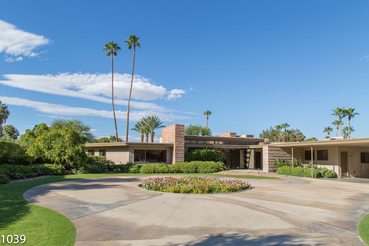 Mid-century modern ranch home with circular driveway, manicured landscaping, and tall palm trees in Palm Springs.