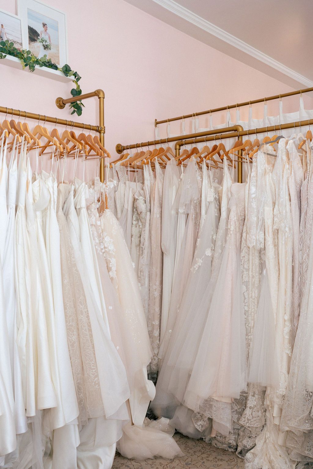 Elegant white wedding dresses and gowns hanging on brass racks in Lace & Liberty boutique.