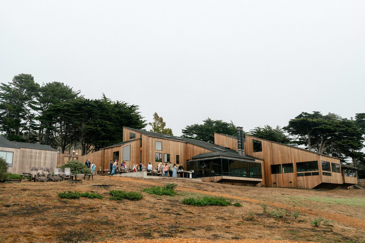 Modern wooden building surrounded by trees on a foggy day with guests gathered outside for an event.