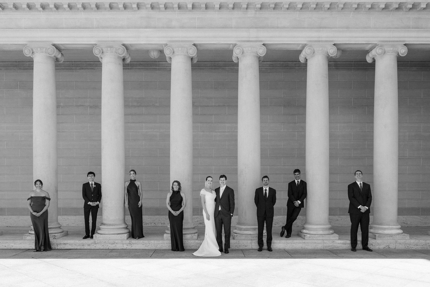 Black and white wedding party photo at Jefferson Memorial columns, bride and groom centered with attendants spaced apart.