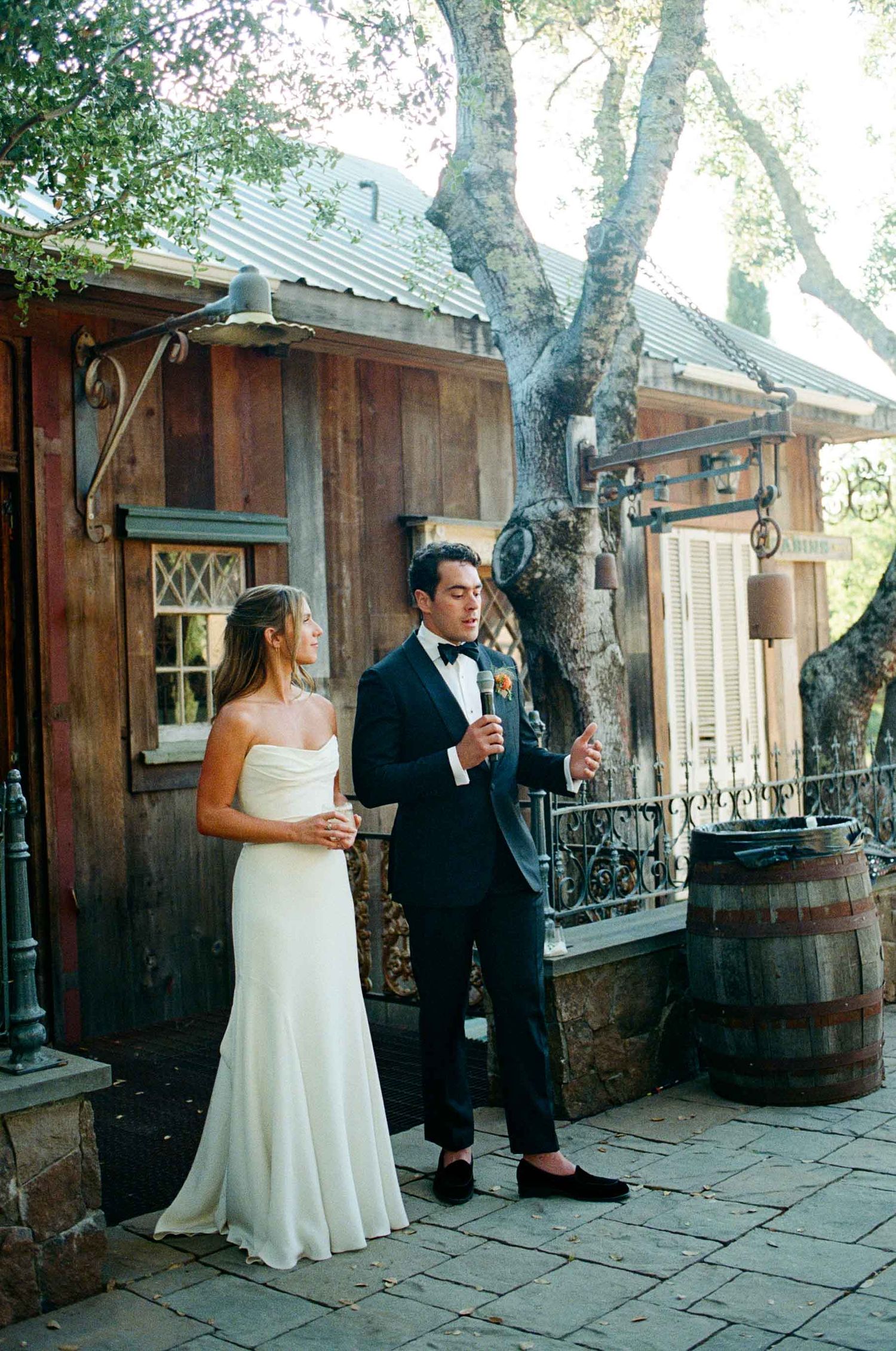 Bride and groom in elegant attire standing outside a rustic wooden venue after wedding.
