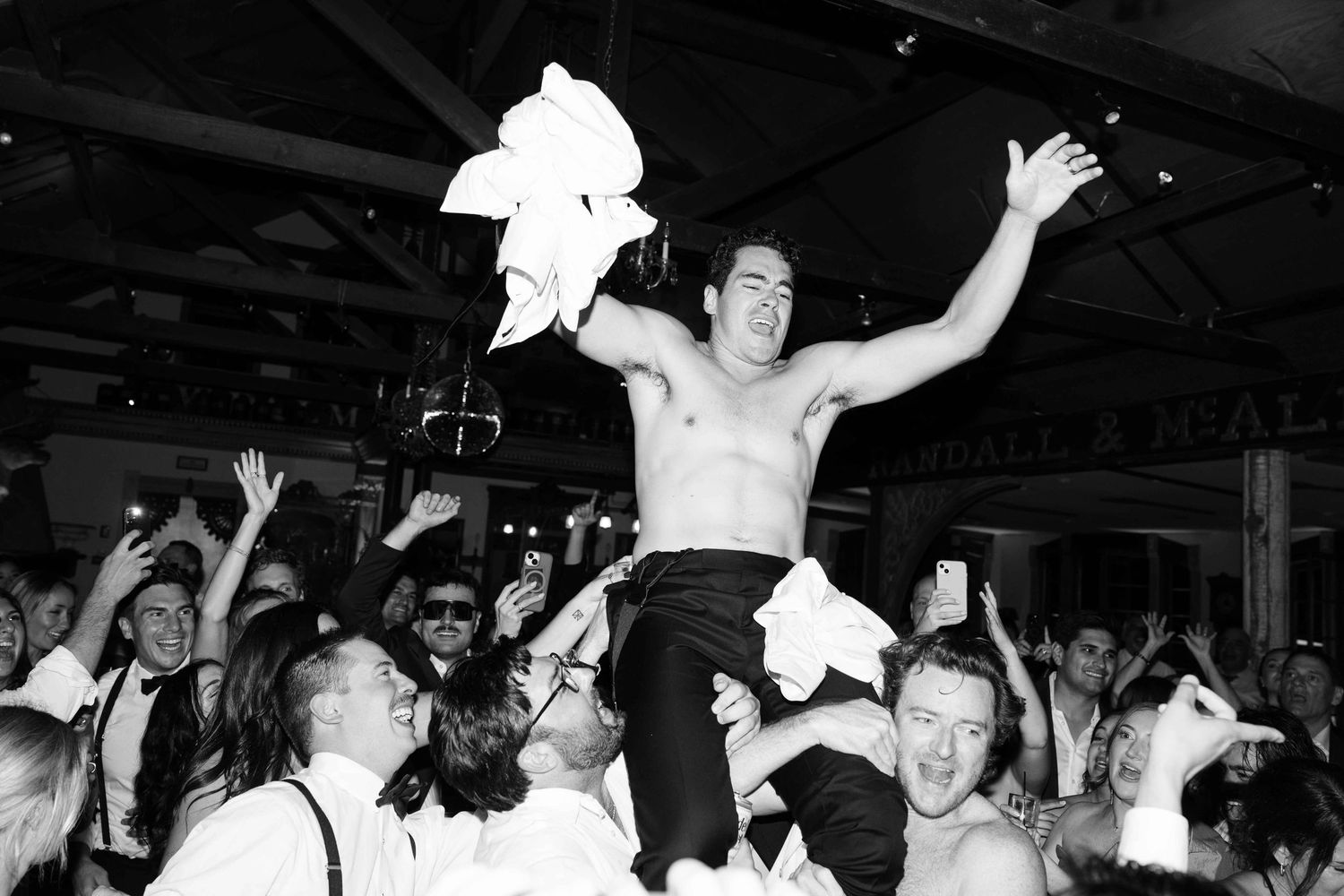 Shirtless groom crowd surfing at lively black and white wedding reception party celebration.