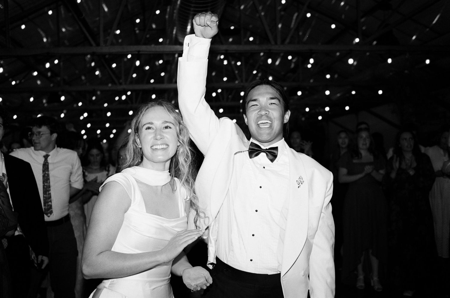 Black and white photo of bride and groom celebrating on wedding dance floor, groom raising fist in joy.