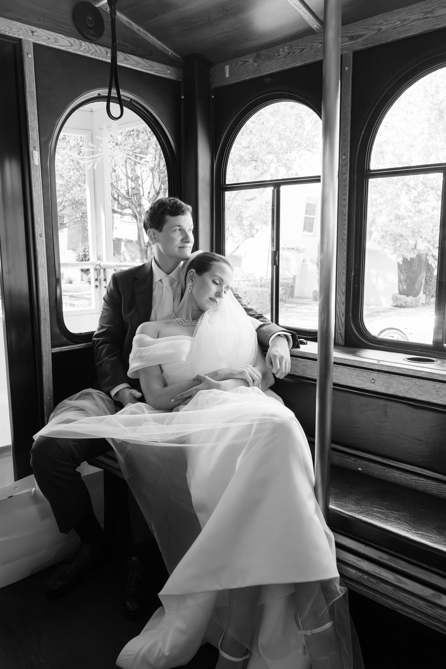 Black and white photo of a bride and groom sitting together on a vintage trolley, sharing a tender moment.
