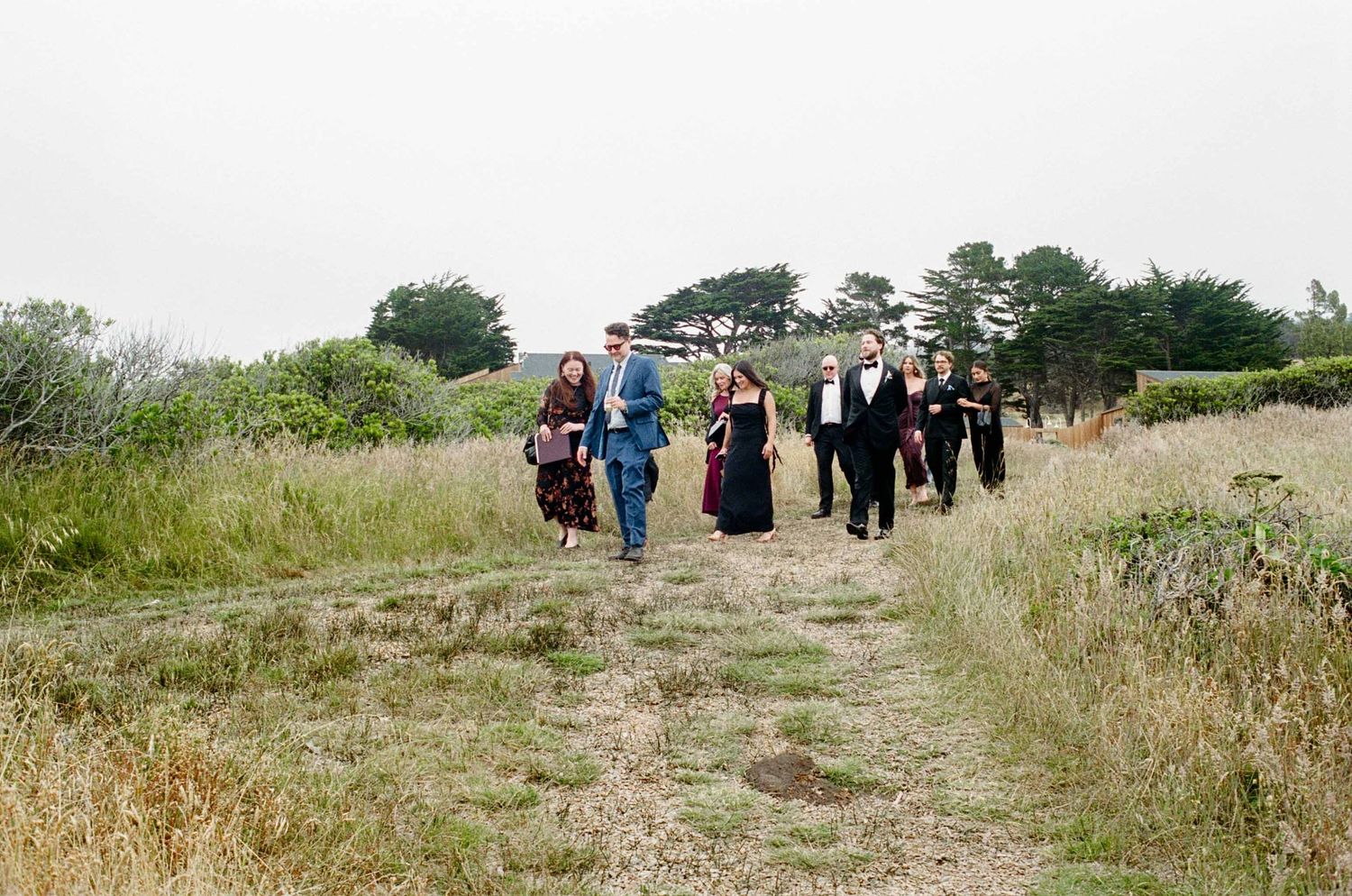Group of people walking along a grassy path through open fields on a cloudy day.