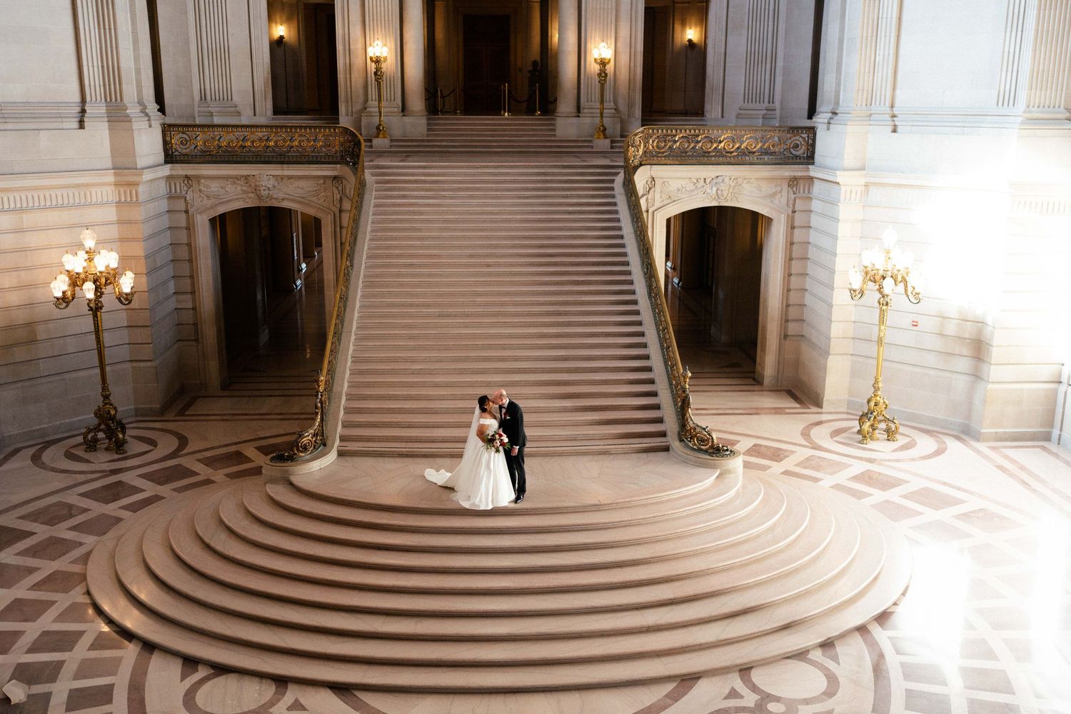 Wedding couple stands on grand marble staircase City Hall.