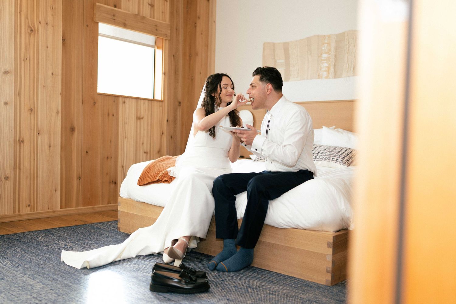 Bride and groom sitting together on a bed in a wood-paneled room, sharing an intimate moment on their wedding day.