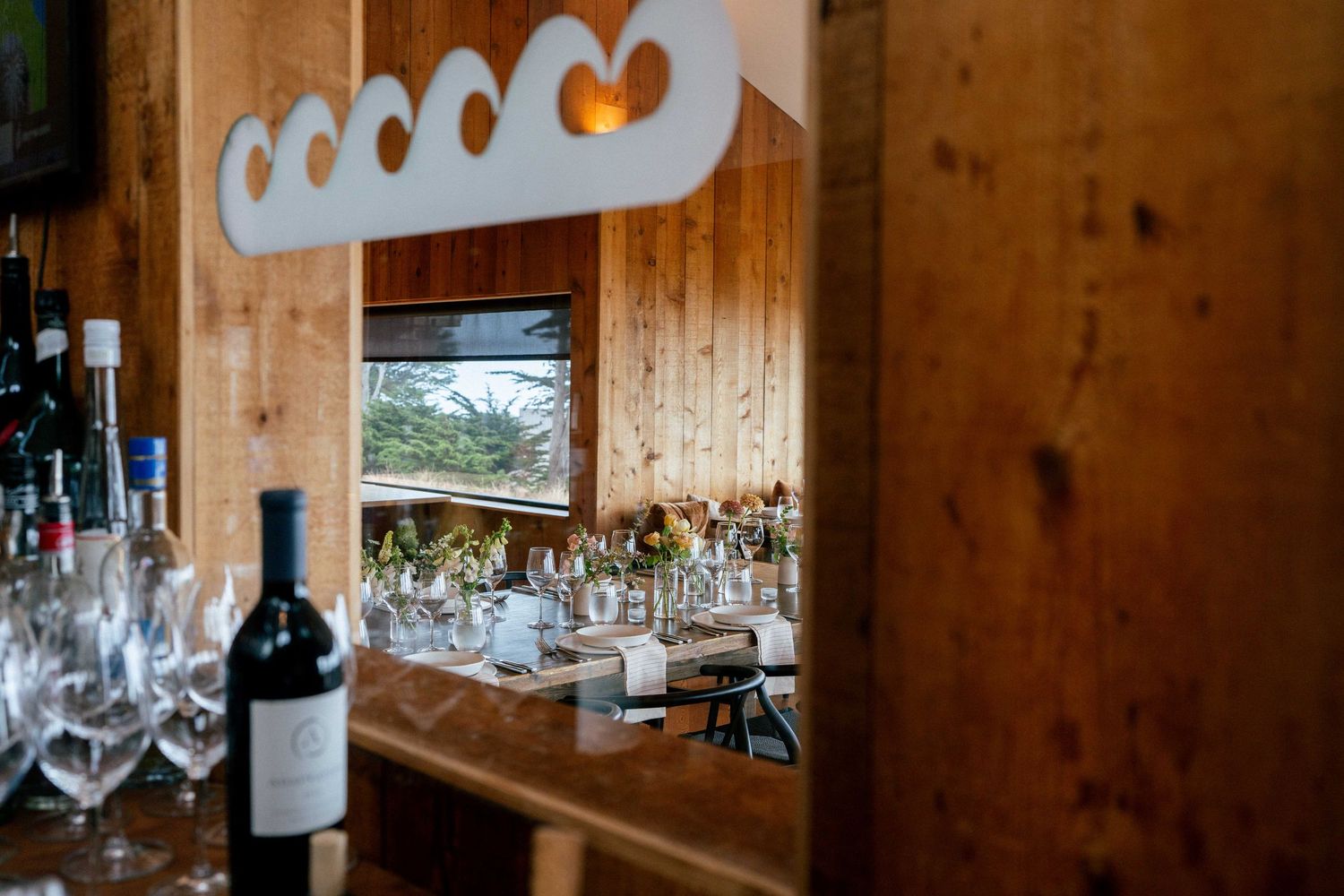 Rustic wooden bar with wine glasses and a bottle of red wine reflected in a decorative mirror.