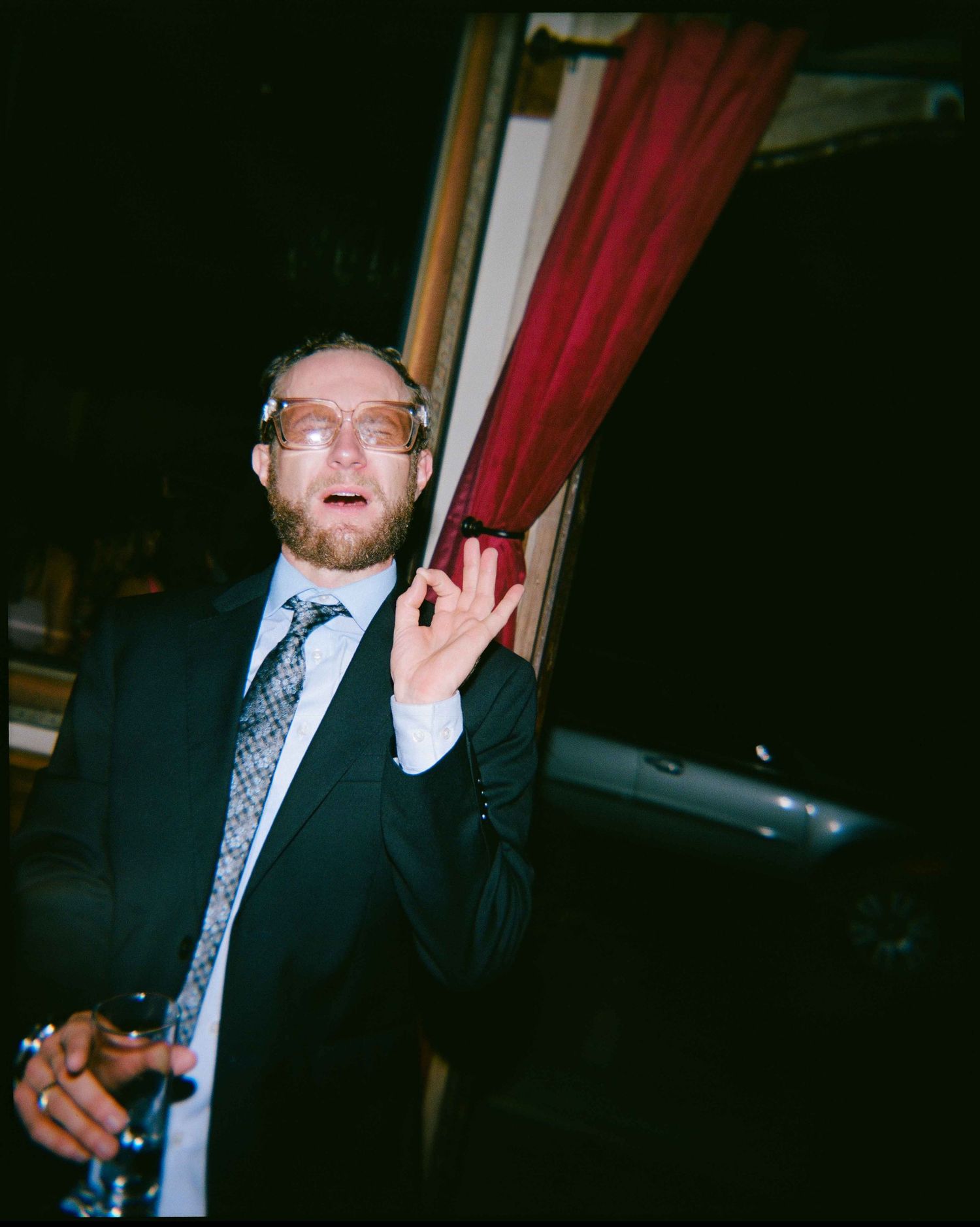 Man in a suit wearing novelty glasses makes an OK gesture at a wedding reception.