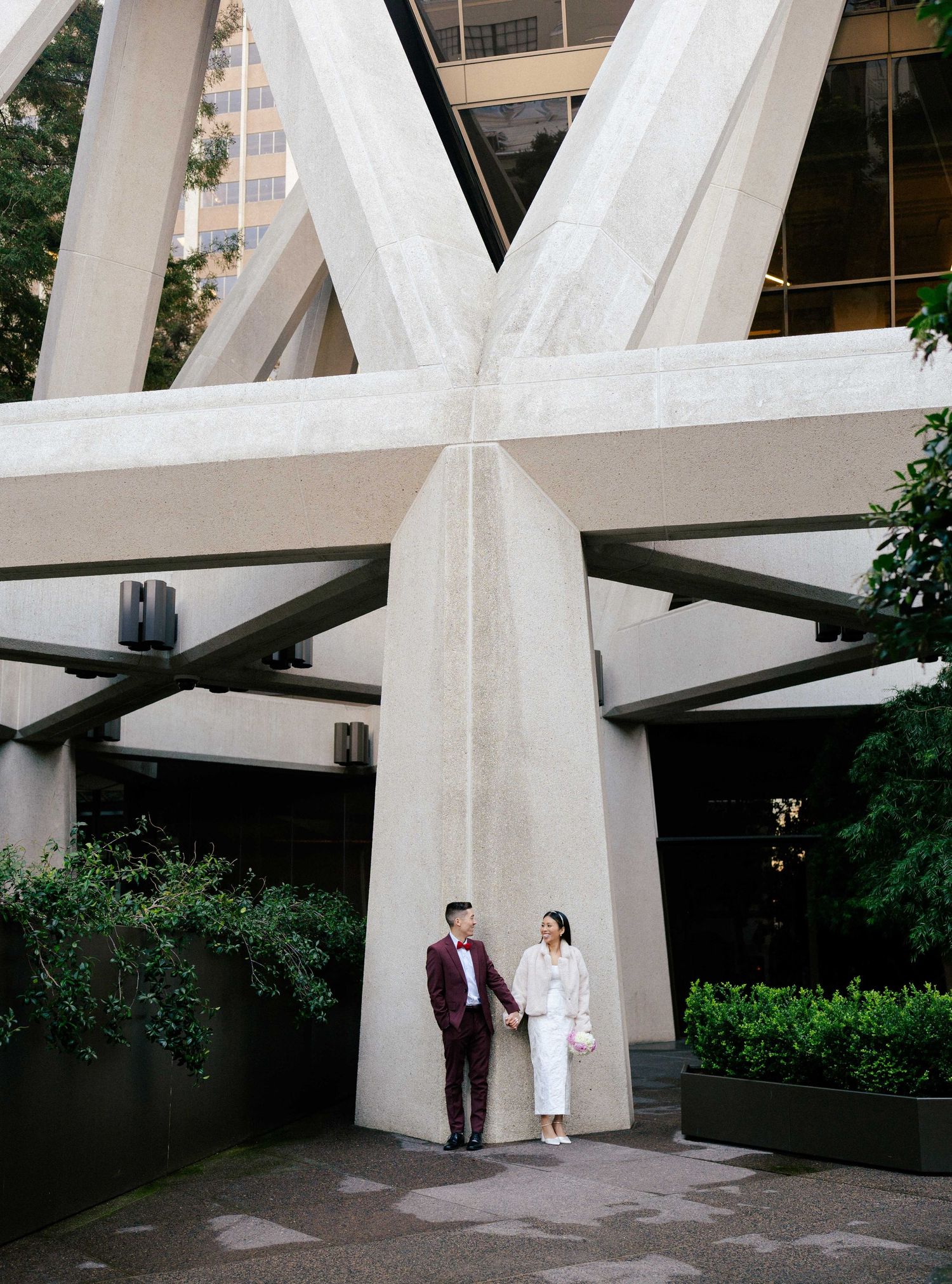 A wedding photo under the Transamerica Pyramid's white cross-beam architectural structure surrounded by greenery.