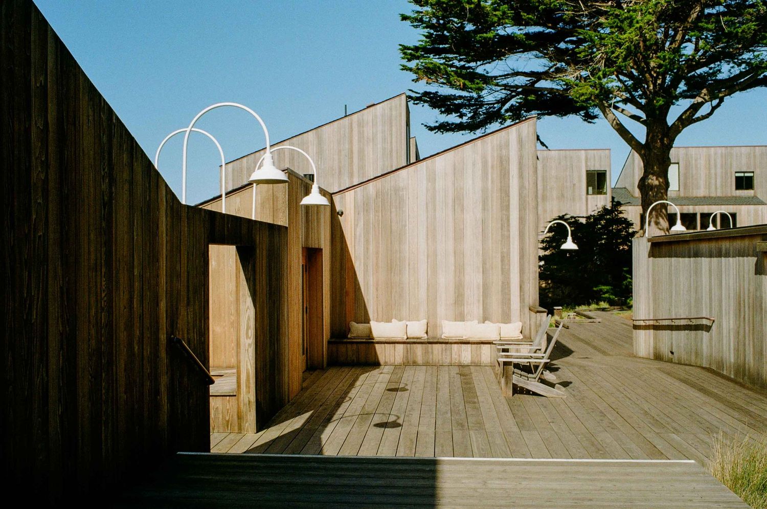 A wooden deck and walkway with minimalist architectural features and curved metal railing against a blue sky.