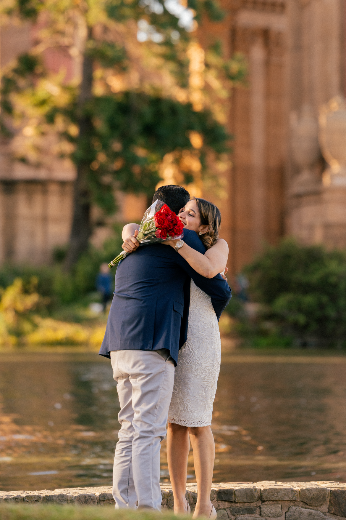 A couple embraces while holding red roses at the Palace of Fine Arts.