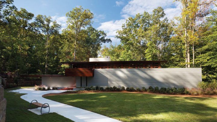 Stunning mid-century modern home with flat roof and concrete facade nestled among mature trees with manicured lawn.