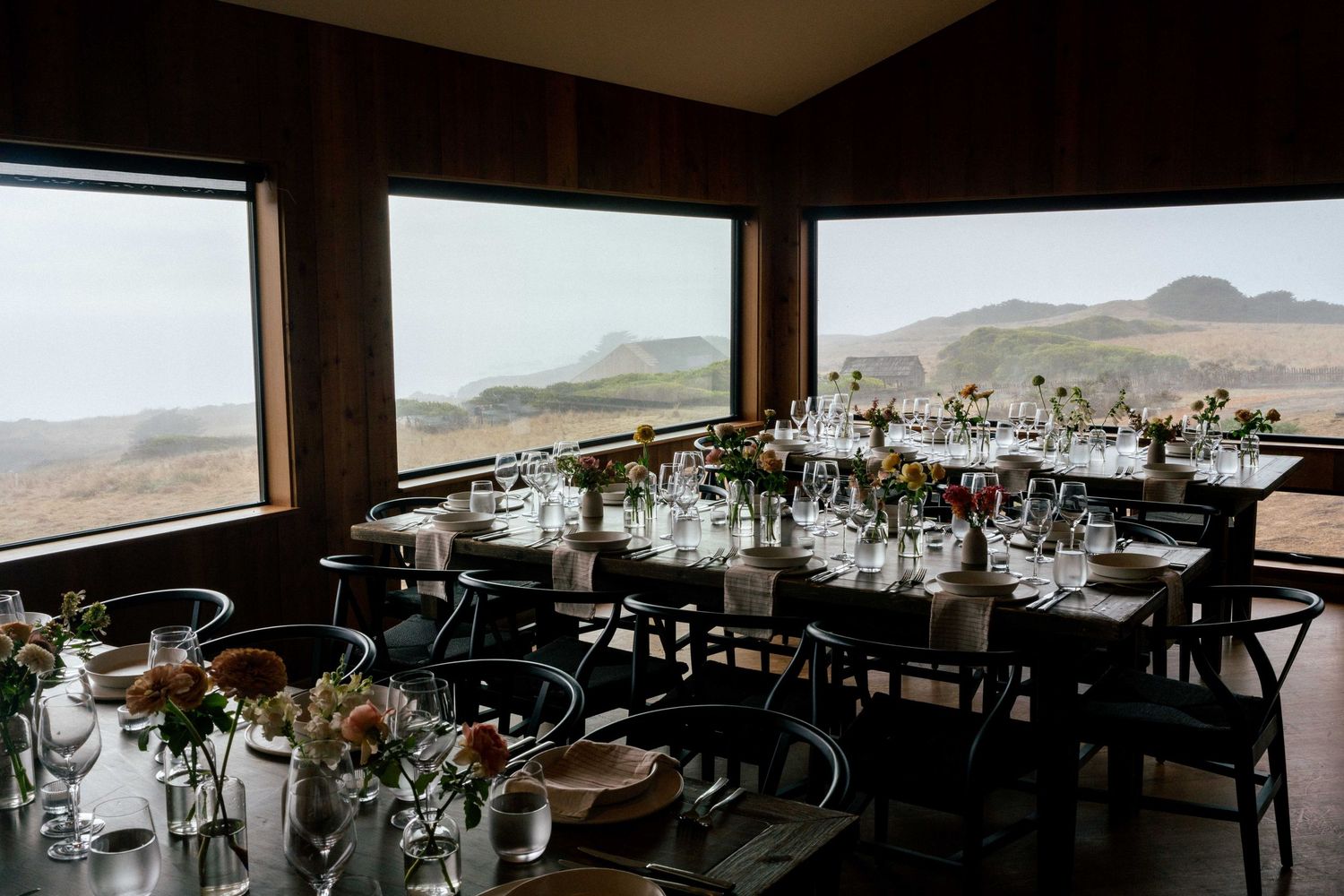 Elegant wedding reception setup with long dining tables, floral centerpieces, and panoramic views of rolling hills.
