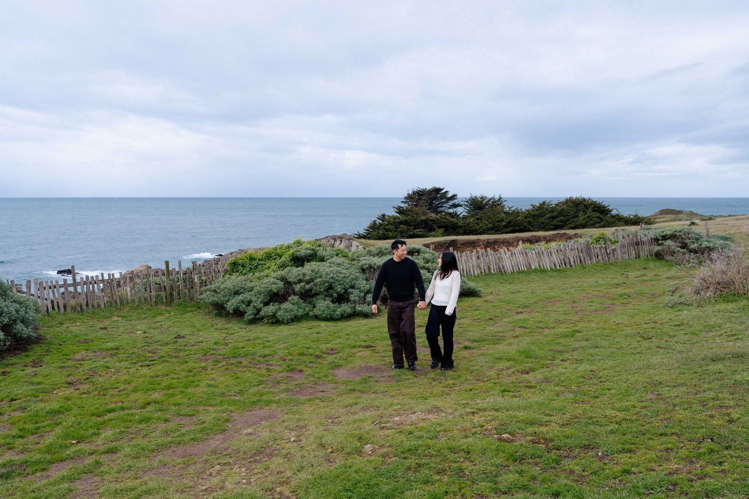 Couple walking on green coastal cliffs overlooking the ocean on a cloudy day.