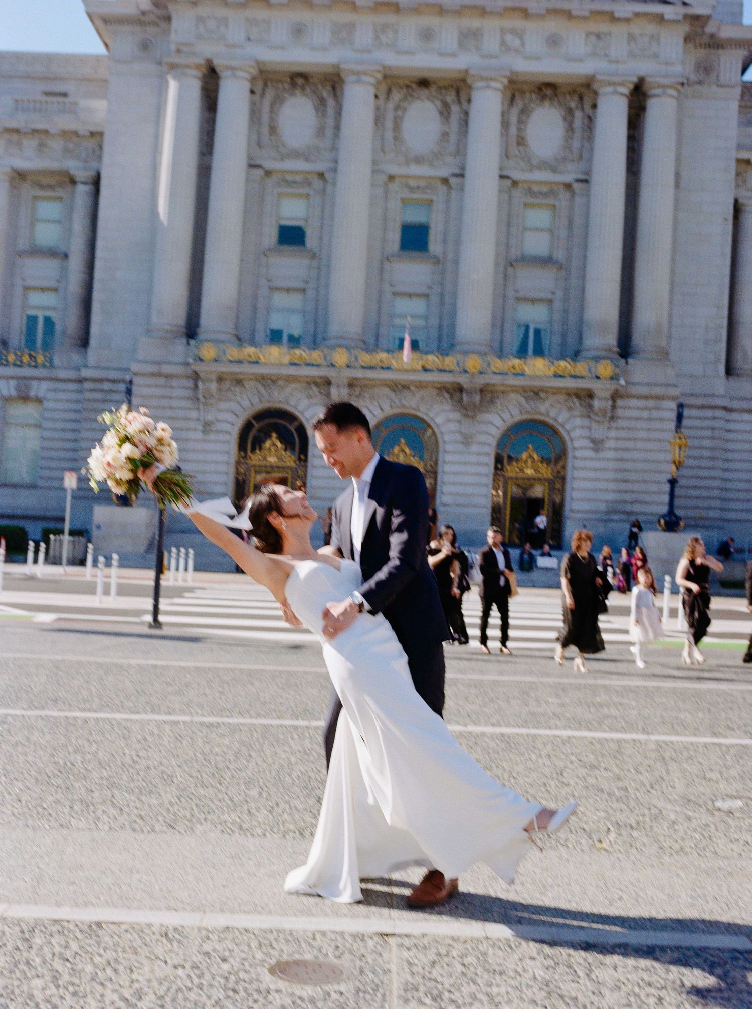 Dynamic wedding pose in front of San Francisco City Hall holding floral bouquet.