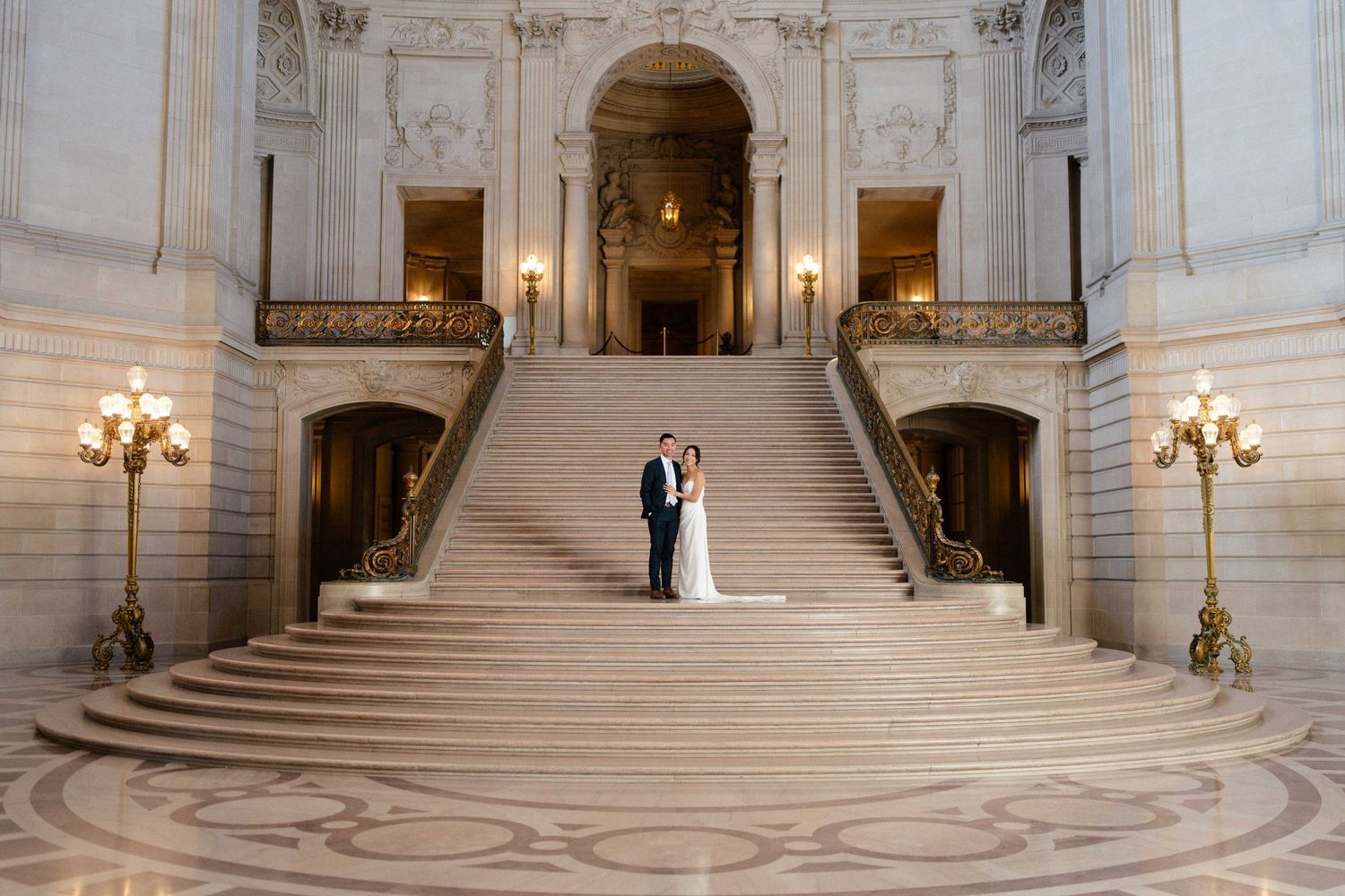 A couple stands at the base of a grand marble staircase in SF City Hall.