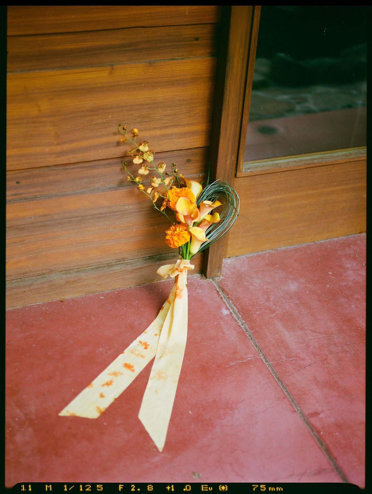 Small orange bouquet sitting next to wooden exterior.