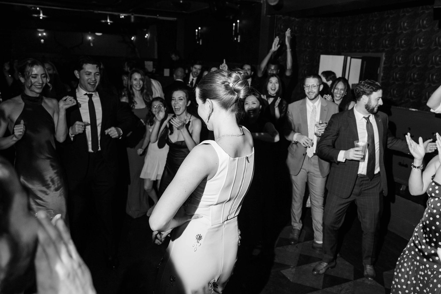 Black and white photo of guests dancing at a lively wedding reception party on the dance floor.