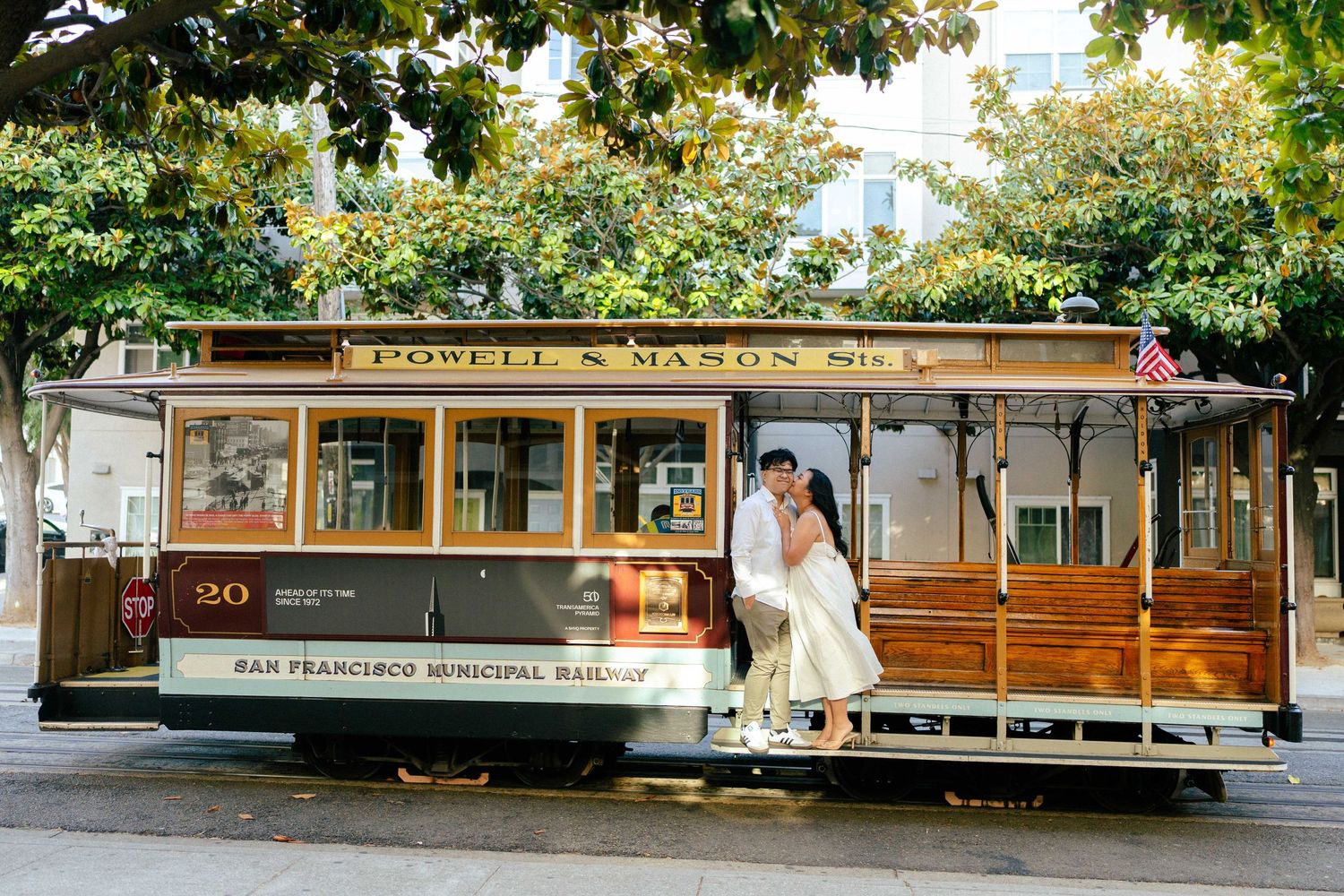Bride in white dress posing on historic San Francisco cable car on sunny day.