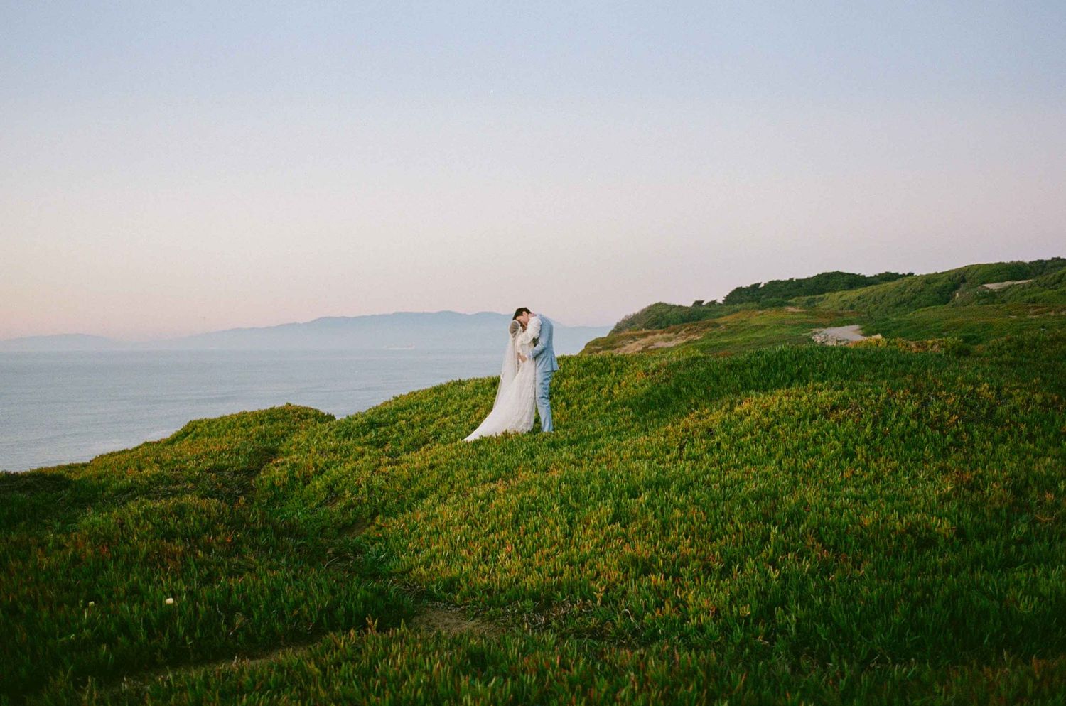 Wedding couple kissing on bluff overlooking the Pacific Ocean.