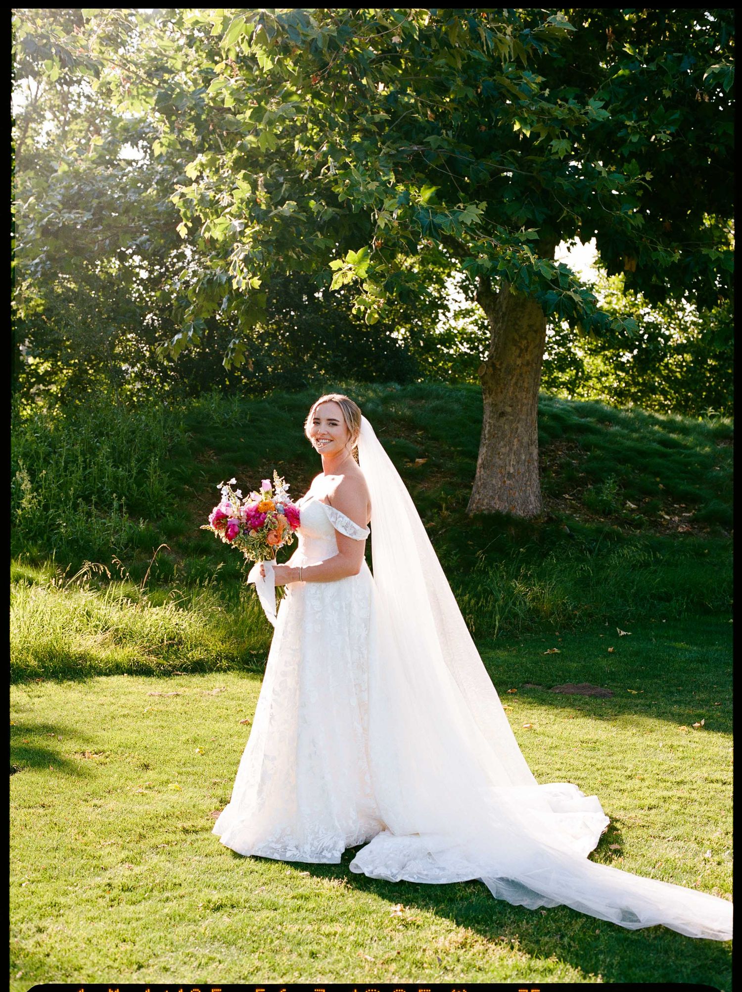 Bride looking over her shoulder with a smile, holding a pink bouquet.