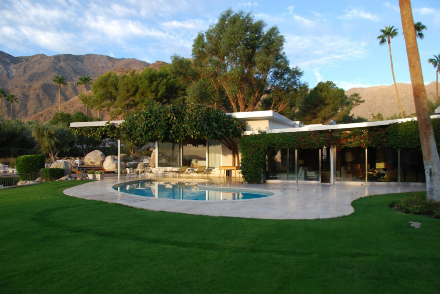 Mid-century modern Palm Springs home with flat roof, kidney-shaped pool, and mountain views at dusk.