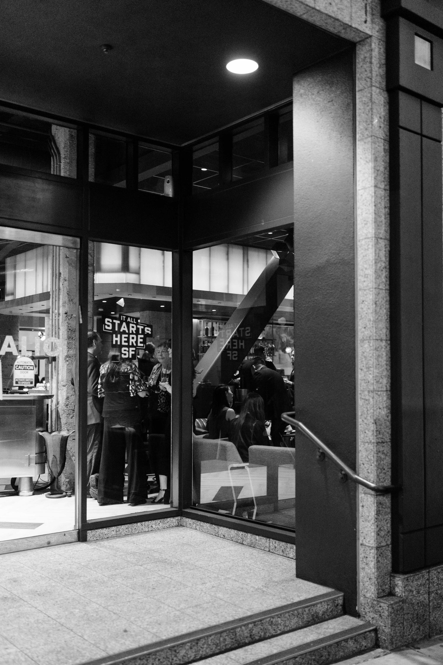 Black and white photograph of a modern storefront entrance at night.