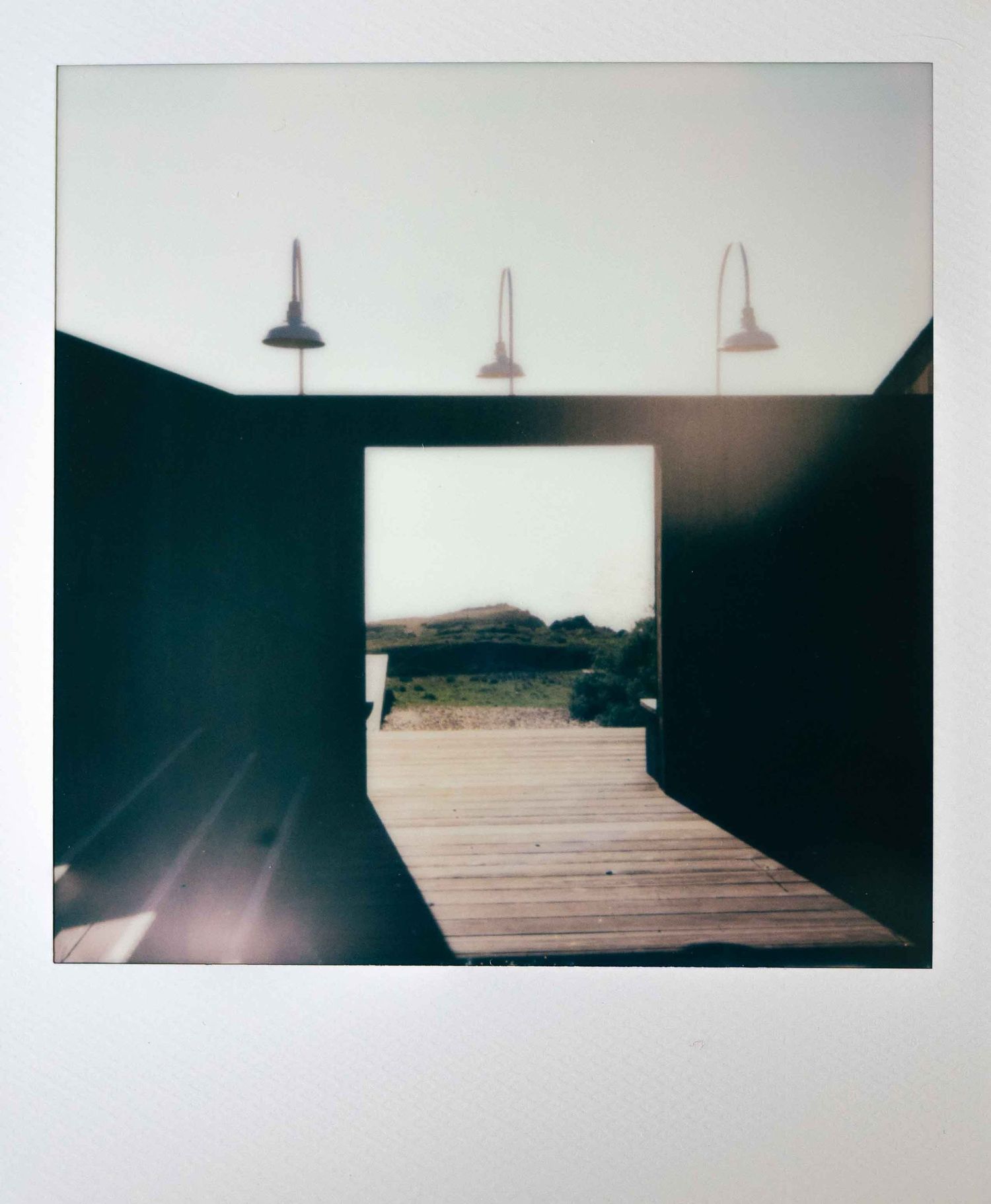 Polaroid photo of mid-century modern wooden portal overlooking the Pacific Ocean at sunset.