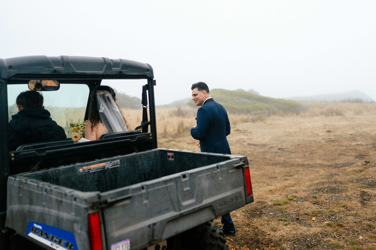 Bride and groom near a utility vehicle in a misty field on their wedding day.
