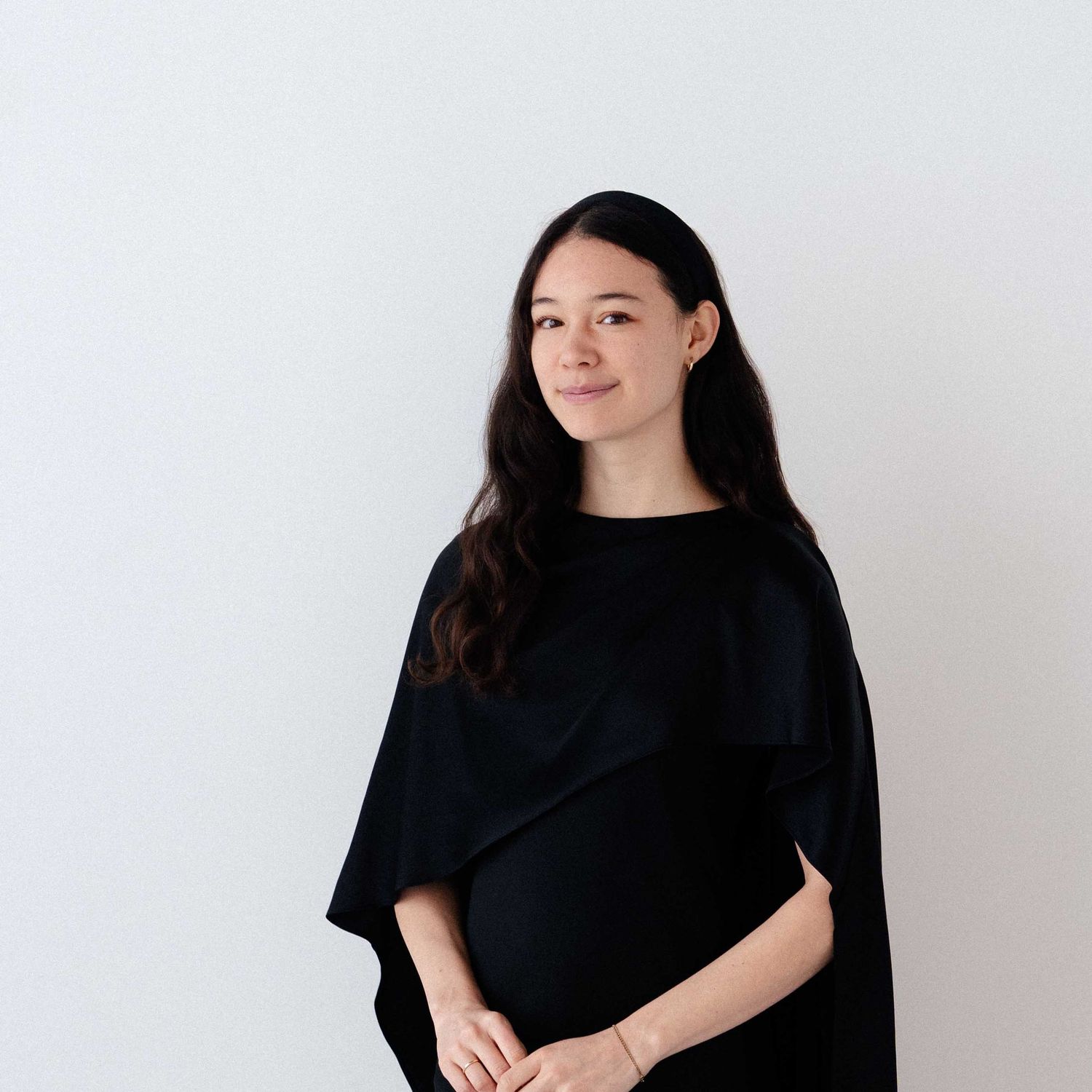 Pregnant woman with long dark hair in a black top smiling against a white background.