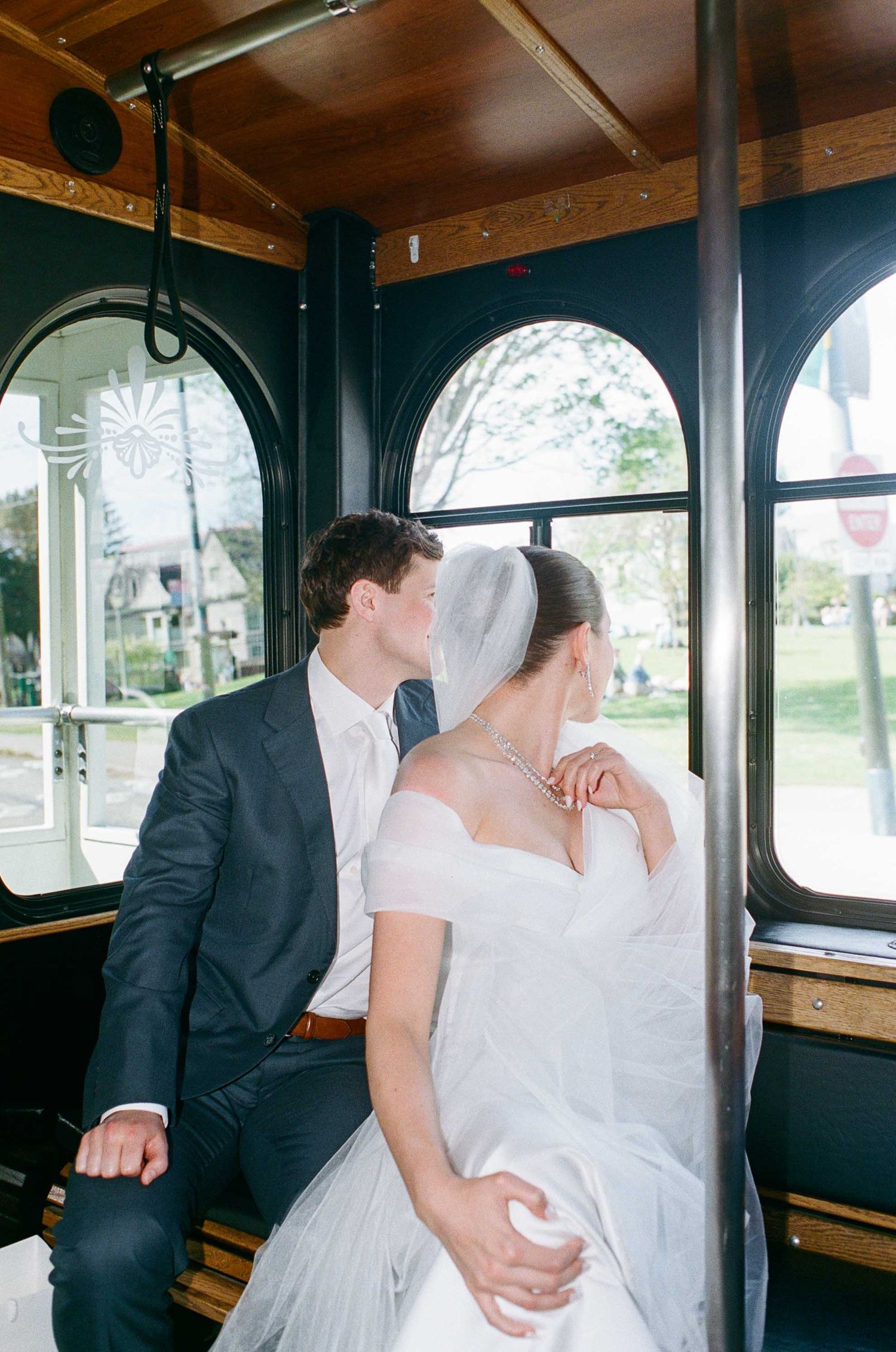 A bride and groom share a romantic moment on a vintage trolley, with the bride in a white gown and veil leaning into her groom.