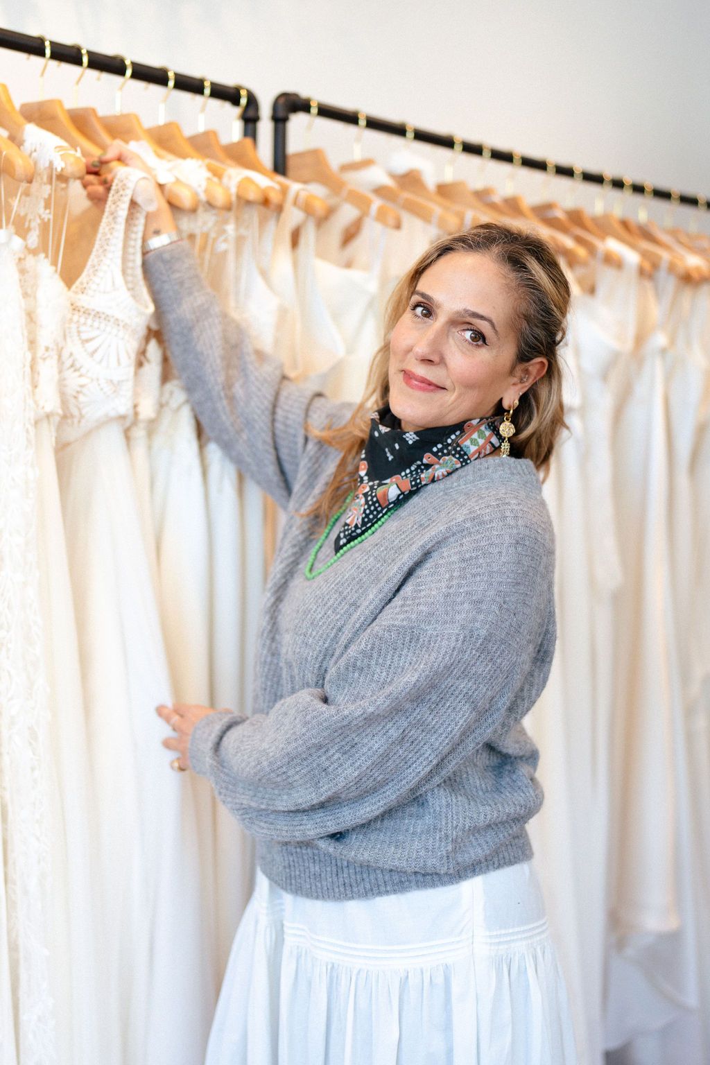 Samira, WildBride boutique owner, in a gray sweater browses through wedding dresses in a bridal boutique.
