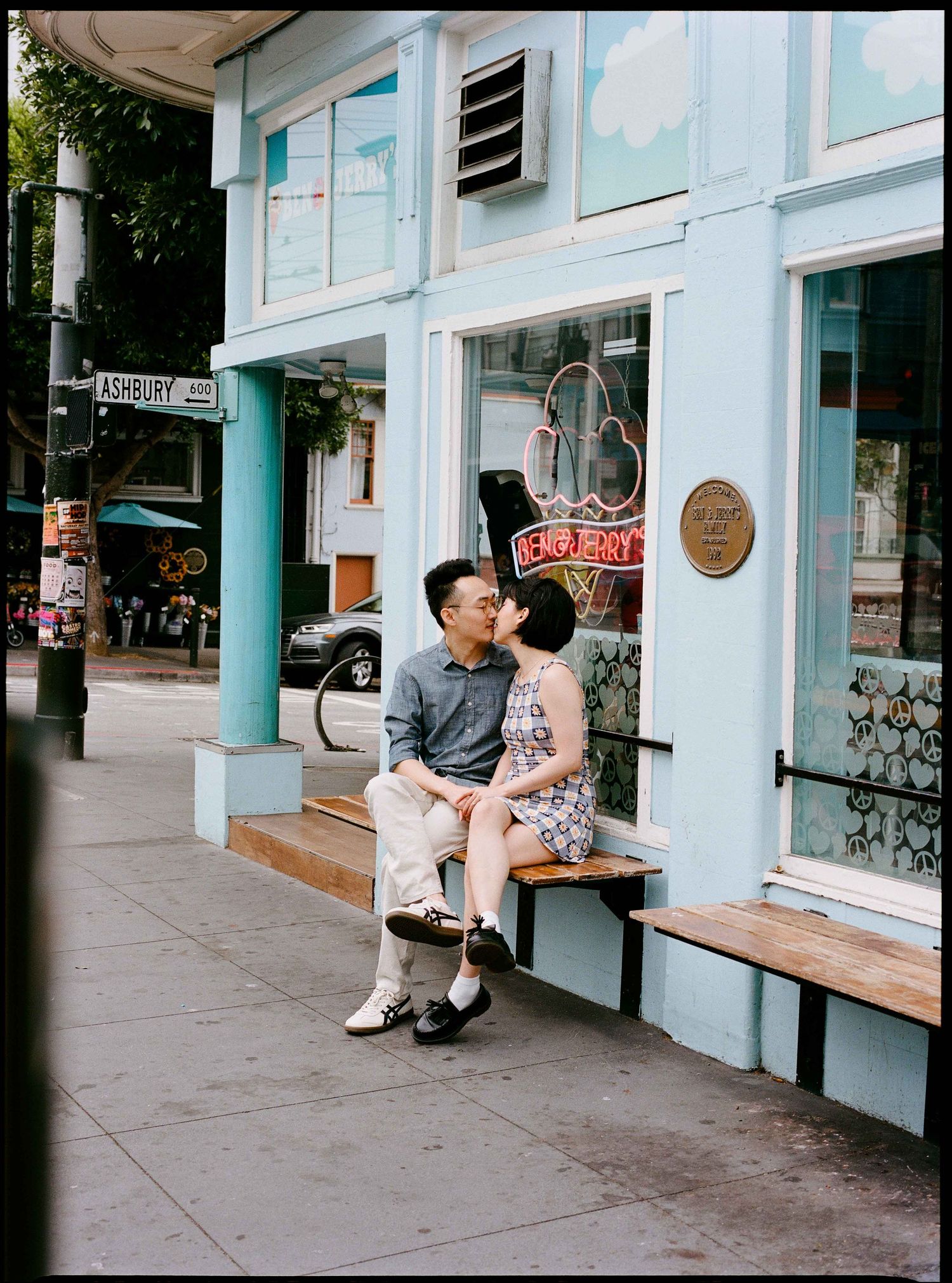 Couple shares kiss on bench outside colorful Ashbury Street storefront in San Francisco.
