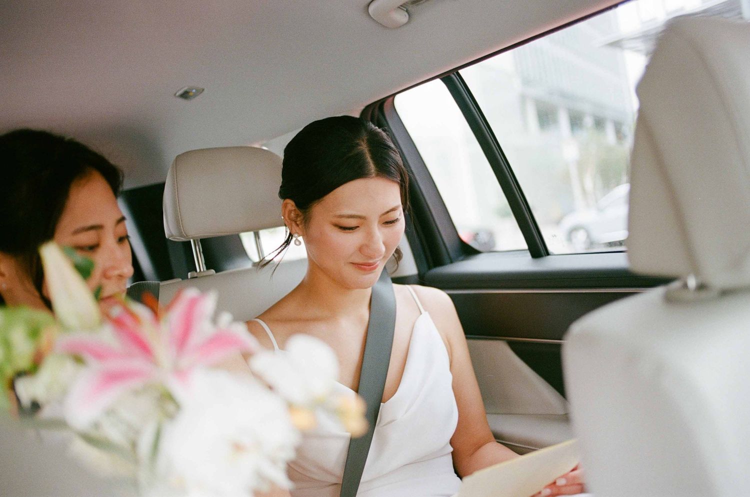 Bride reading letter in a car while her friend looks at her.