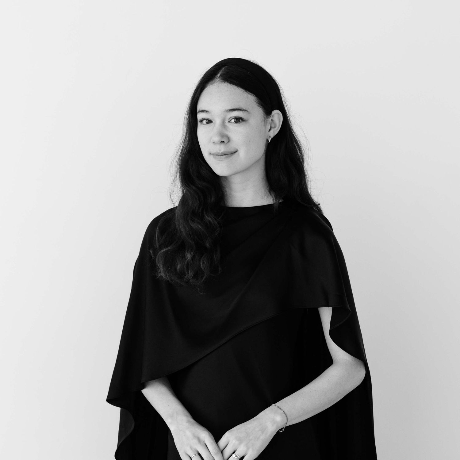 Black and white portrait of a young woman with long dark hair wearing a black cape top.